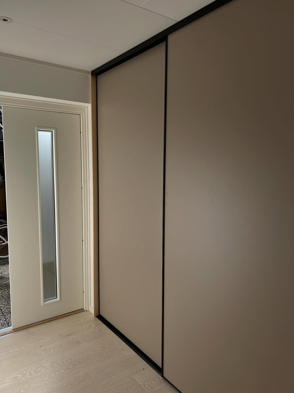 Skjutgarderober med beige dörrar och svarta profiler i en hall intill entrédörren
