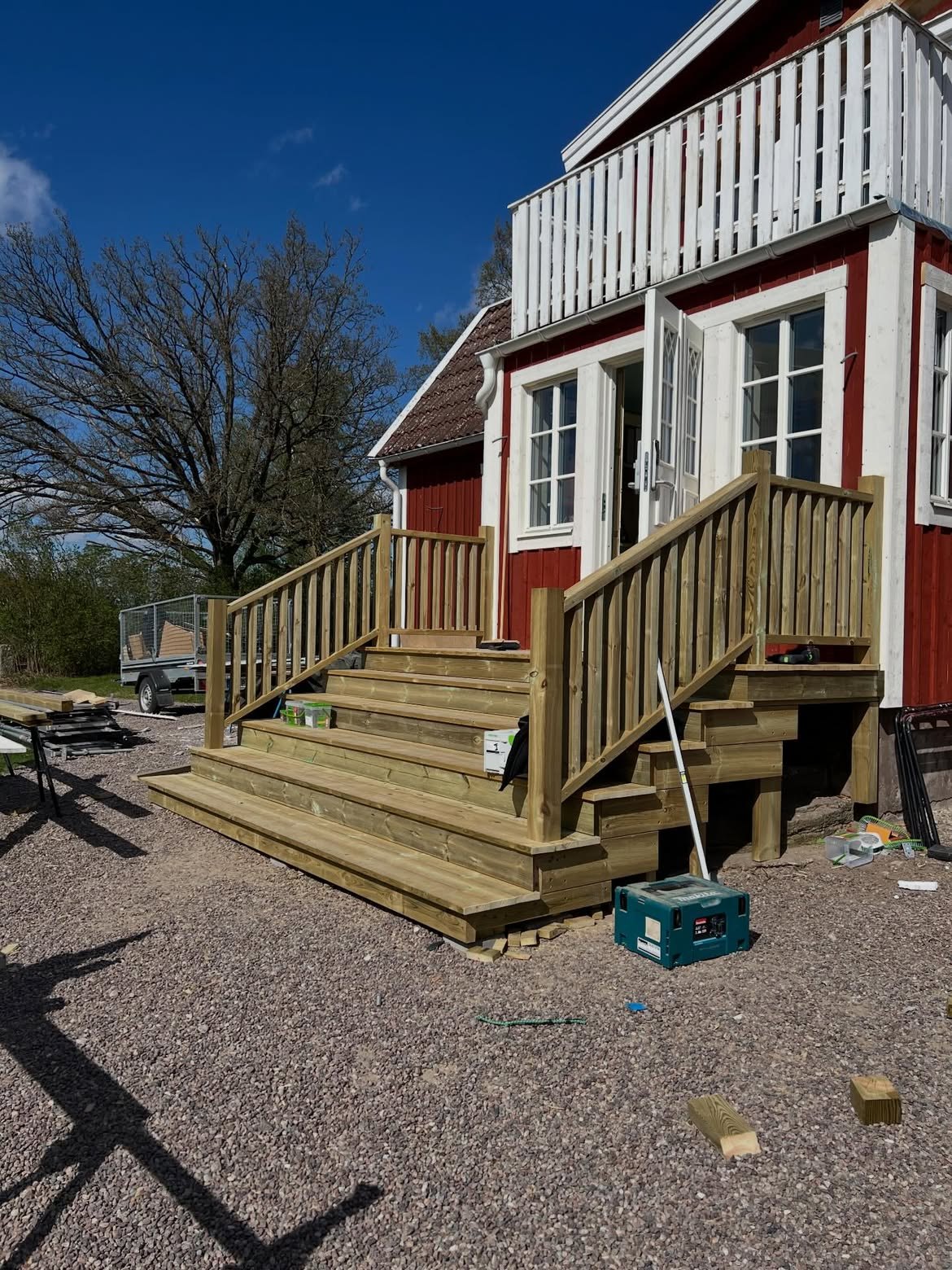 Nybyggd altan med bred trappa och räcke i trä framför en röd villa