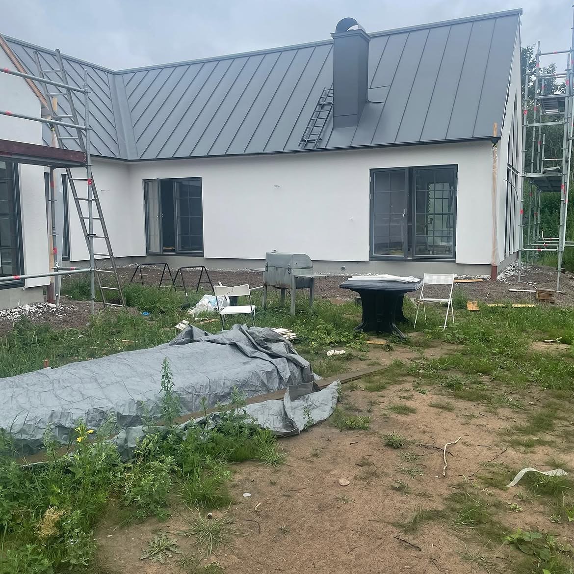 Nybyggt vitputsat hus i Kolboda med grått falsat plåttak och byggställning kvar