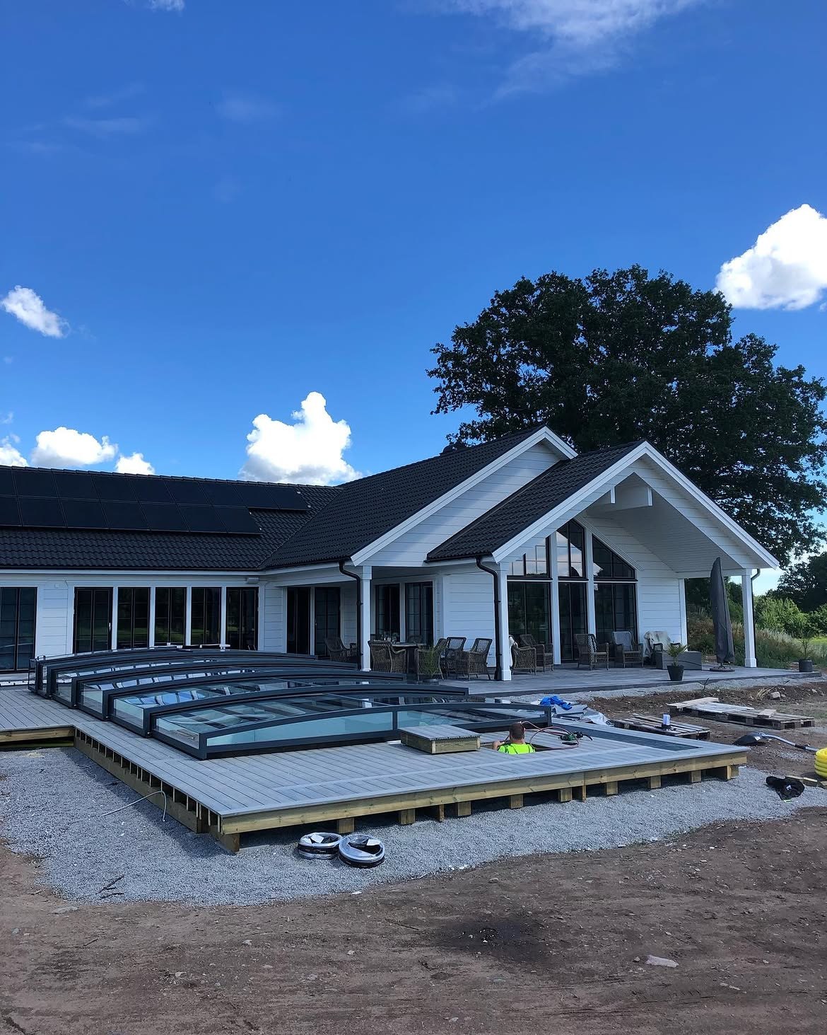 Nytt altandäck i ljus komposit kring en pool med skjutbart poolöverdrag vid en vit villa