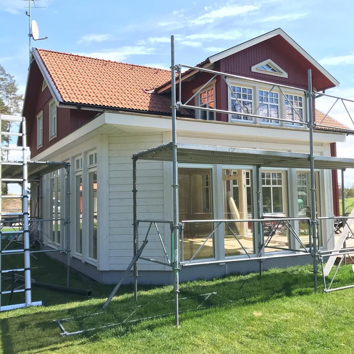 Nybyggt uterum med vit träpanel och stora glaspartier vid ett rödmålat hus i Krankelösa